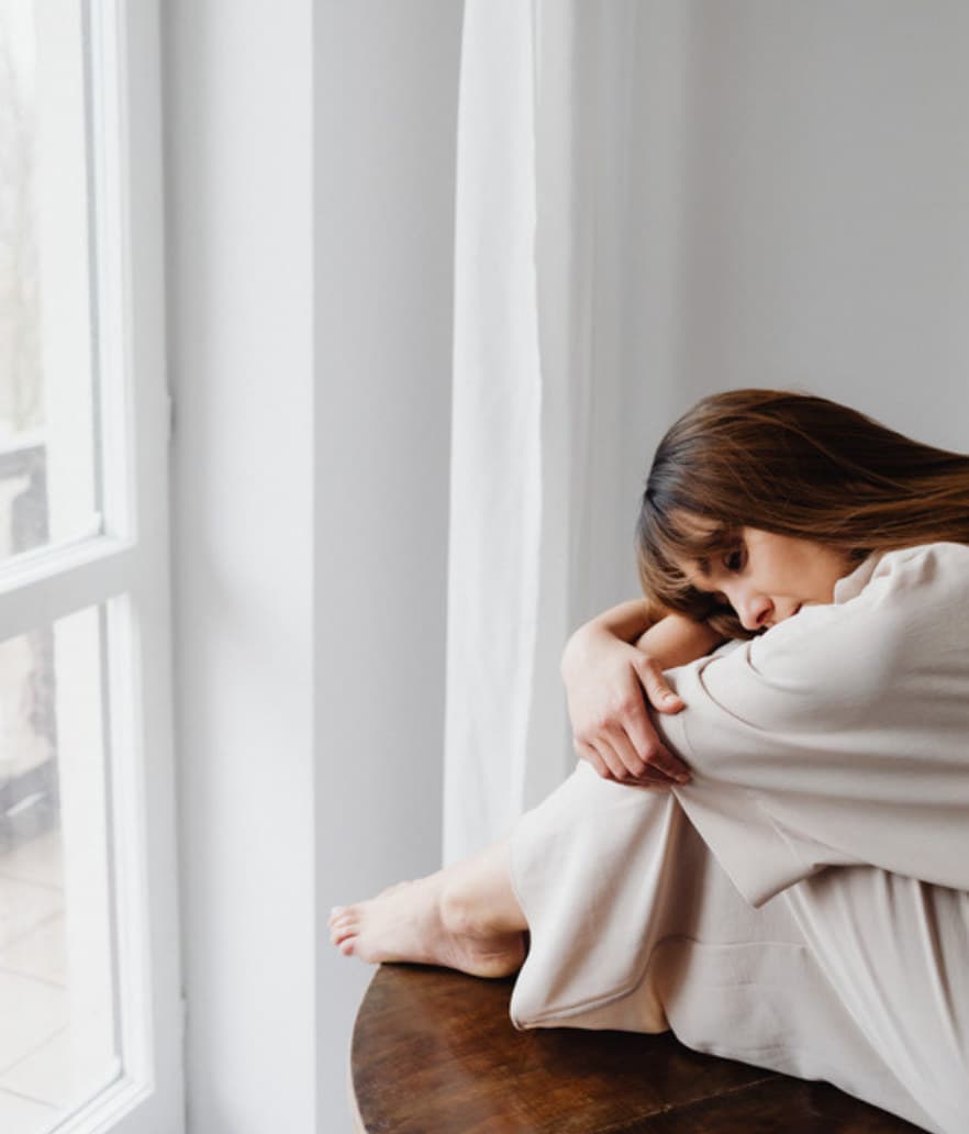 A woman curled up by the window with her grief
