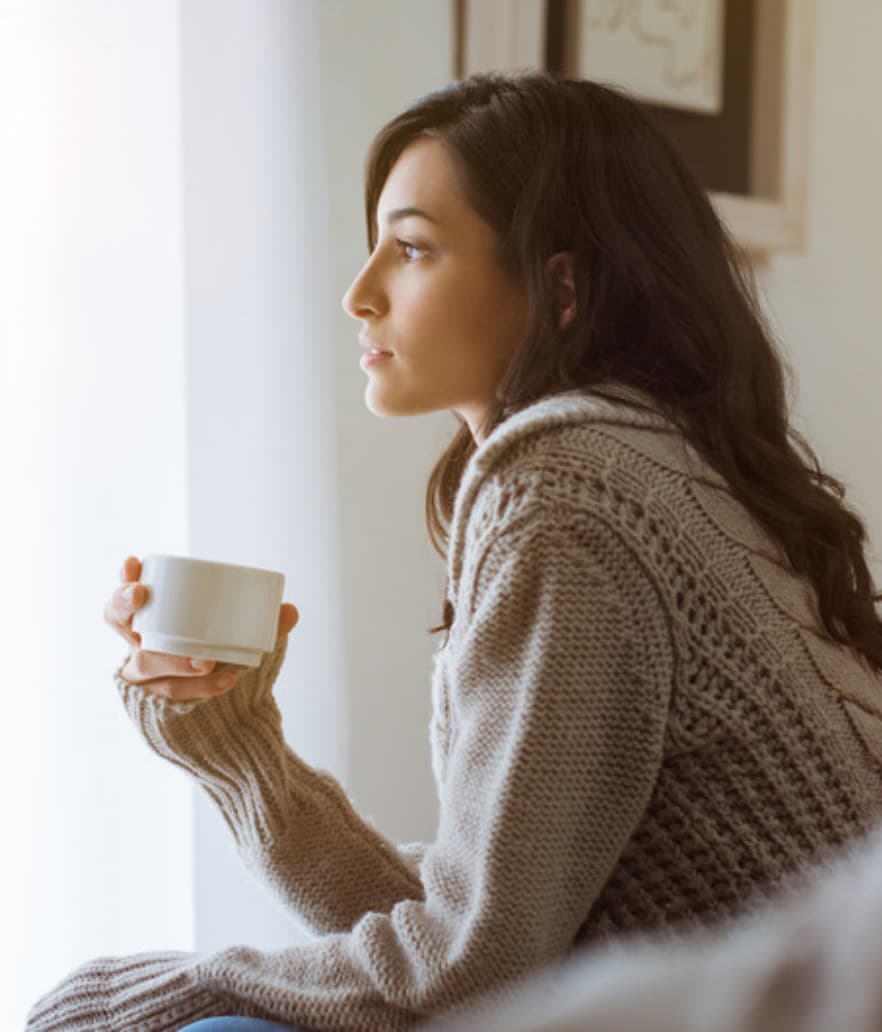 A woman in her forties sitting with a warm drink and her thoughts