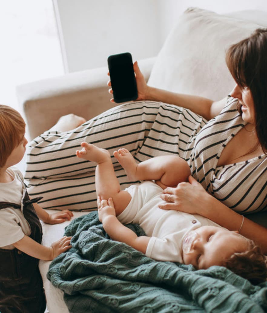 A working mom checking her phone with her kids piled beside her