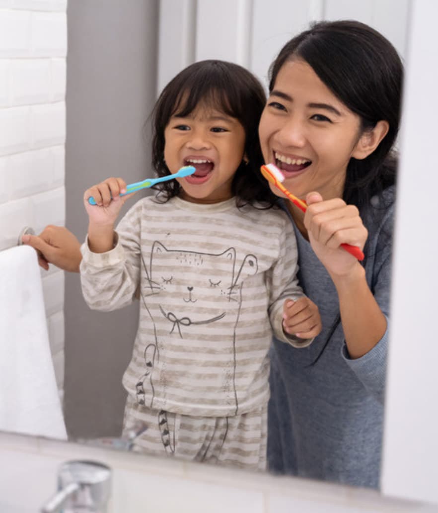 A mom and her toddler brushing teeth together