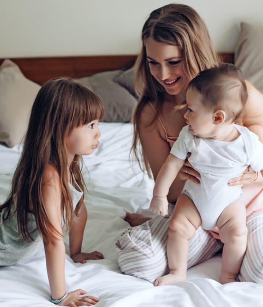 A mom on the bed with her toddler and baby