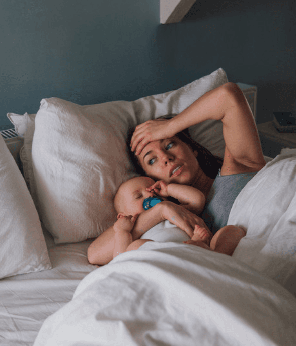 A mom lying in bed beside her baby, drained