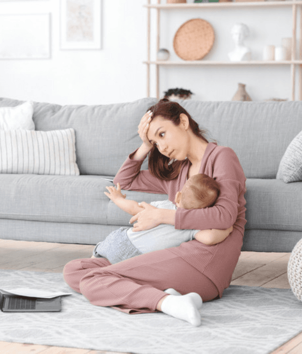 A mom on the floor holding her baby, looking exhausted