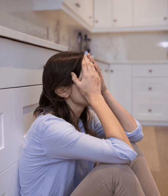A mom sitting on the floor with her hand to her head in an overwhelmed moment