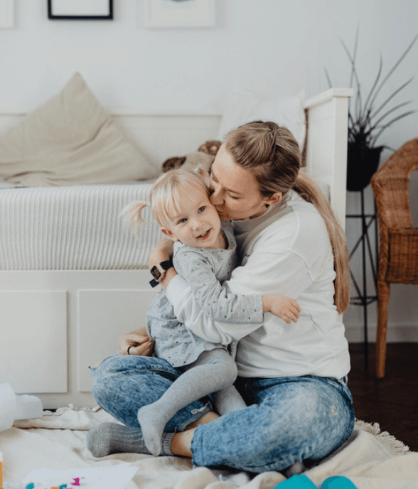 A mom kissing her young daughter in a warm embrace at home