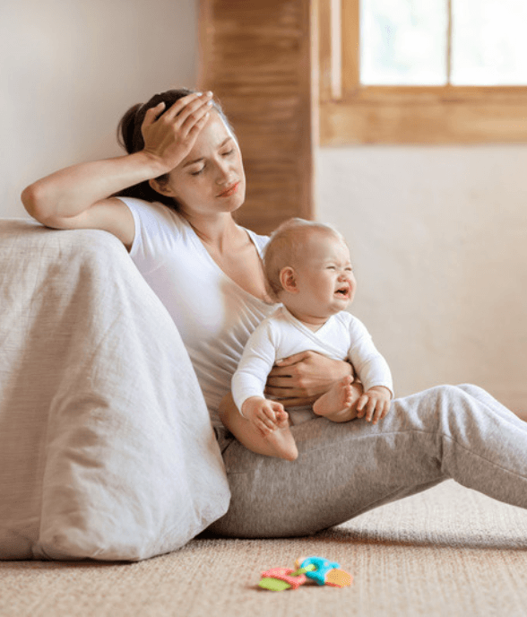 A mom sitting on the floor holding her crying baby, looking overwhelmed