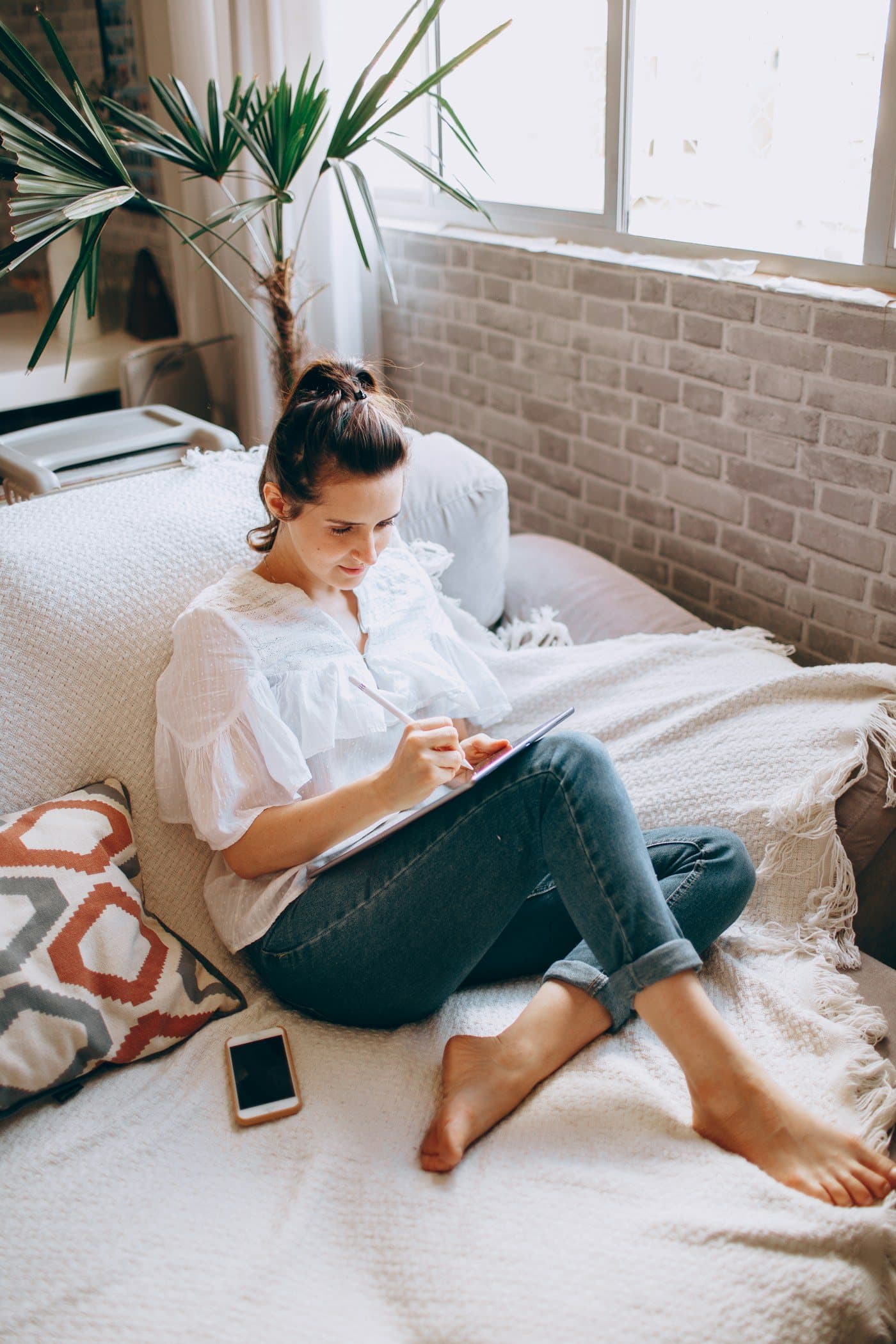 A mom on her bed by the window, reading on a tablet